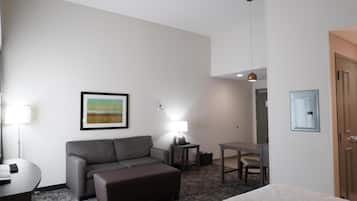 A hotel room with a sofa, a small table, a lamp, a desk, and a bed.