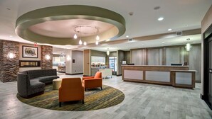 Un vestíbulo de hotel con una recepción, un área de descanso con sofás y sillones, una cocina al fondo y una pared de acento de piedra.
