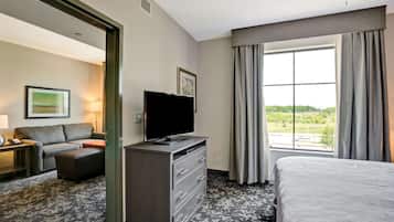 A hotel room with a bed, a TV on a dresser, a sofa, and a large window with curtains.