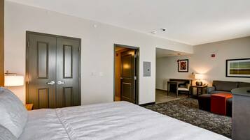 A hotel room with a large bed, a desk with a chair, a sofa, and a small table with a lamp.