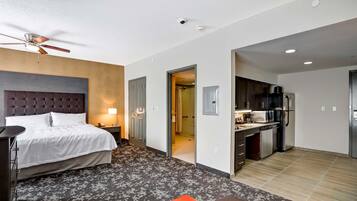 Une chambre d’hôtel équipée d’un lit, d’un bureau, d’une chaise, d’un ventilateur de plafond, d’une salle de bain et d’une kitchenette.