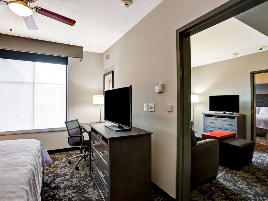 Hotellihuone, jossa on sänky, työpöytä, tuoli, televisio ja näkymä toiseen huoneeseen.