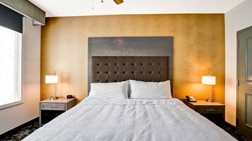 Una habitación de hotel con una cama grande, dos mesitas de noche con lámparas, un ventilador de techo y un ventanal amplio.