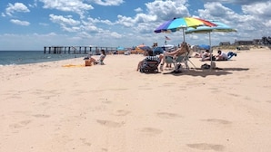 A beach with a pier, umbrellas, and people relaxing.