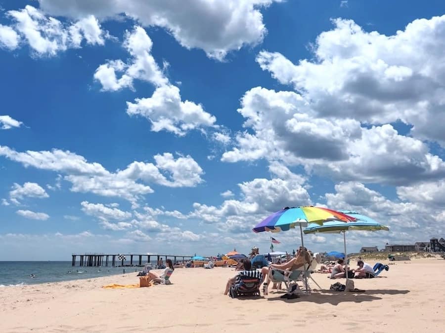 Una playa con un muelle, sombrillas y gente relajándose.