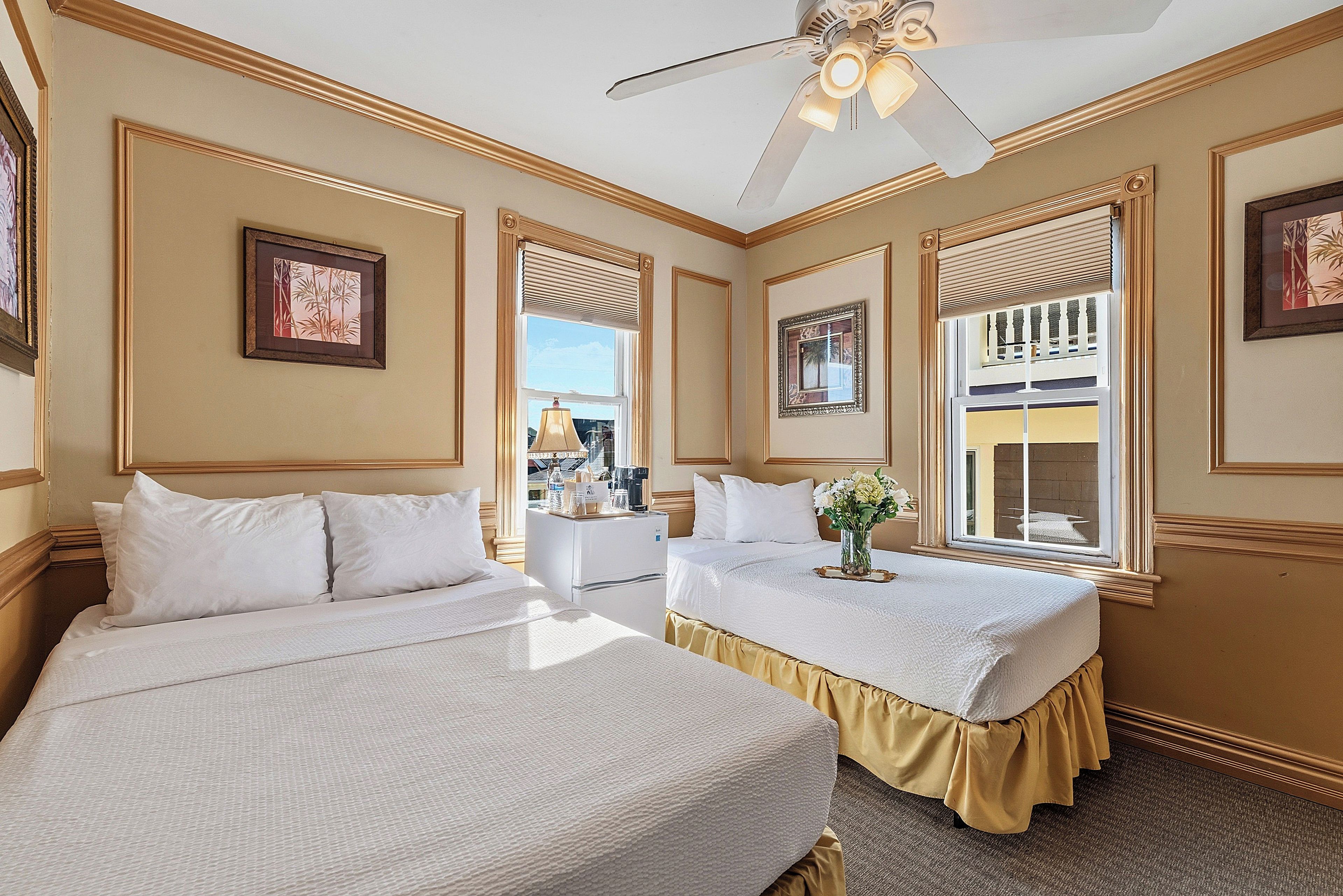 Quarto de hotel com duas camas, um ventilador de teto e vista para o exterior.