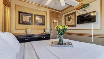 A hotel room with a bed, a dresser, a vase with flowers, a television, and framed artwork on the walls.