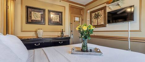 Una habitación de hotel con cama, cómoda, florero con flores, televisor y cuadros en las paredes.
