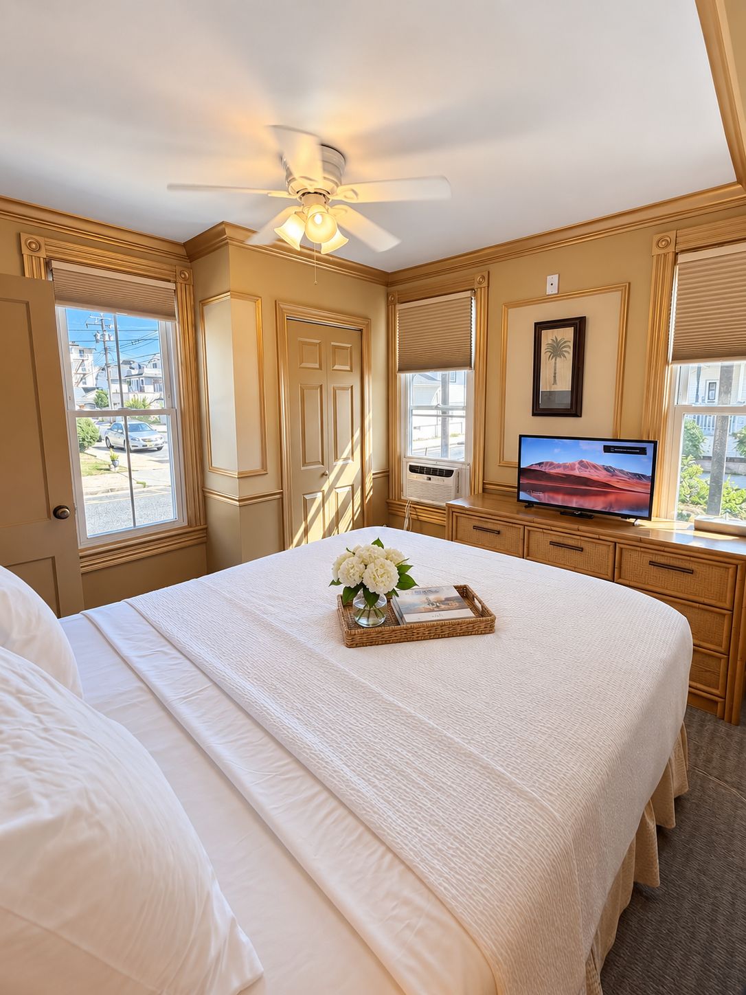 A hotel room with a bed, a television, a ceiling fan, and a window with a view of the outside.