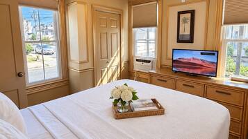A hotel room with a bed, a television, a ceiling fan, and a window with a view of the outside.