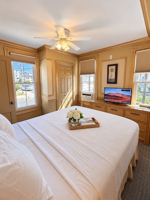 A hotel room with a bed, a television, a ceiling fan, and a window with a view of the outside.