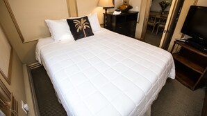 A hotel room with a large bed, a television, a desk with a lamp, and a mirror.