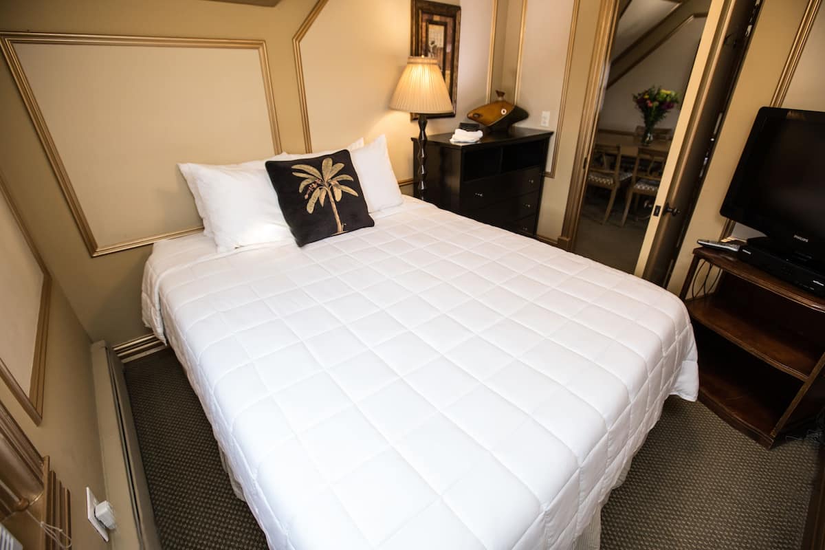 Quarto de hotel com uma cama grande, televisão, escrivaninha com candeeiro e espelho.