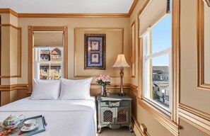 A hotel room with a bed, bedside table, lamp, and a view of buildings outside. - Ocean View Inn (Ocean Grove)