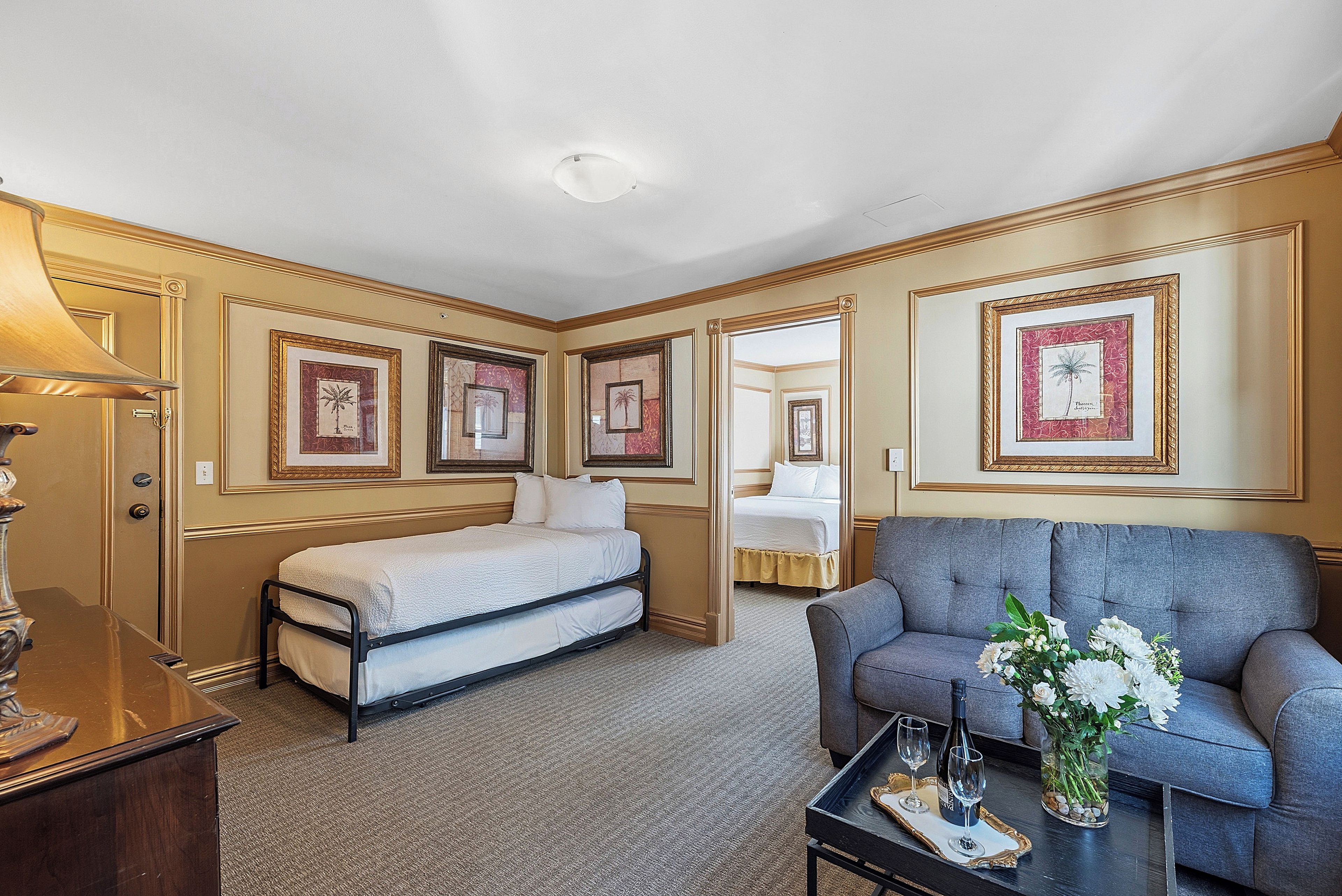 A hotel room with a bed, a sofa, a coffee table with a vase of flowers, and framed pictures on the walls.