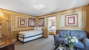 A hotel room with a bed, a sofa, a coffee table with a vase of flowers, and framed pictures on the walls.