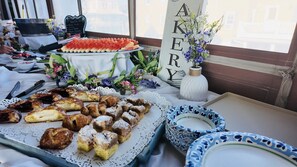 A table with a variety of pastries and a watermelon dish, a vase with flowers, and a sign with the word 'AKERY'.