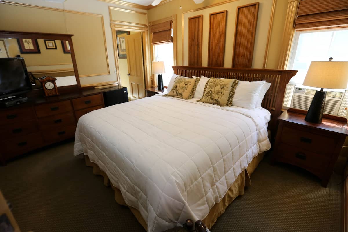 Quarto de hotel com cama grande, cabeceira de madeira, duas mesas de cabeceira com luminárias, cômoda e televisão.