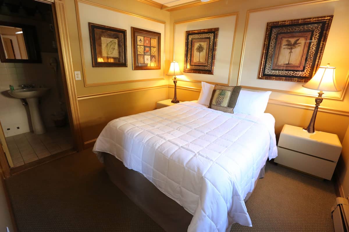 Quarto de hotel com uma cama grande, duas mesas de cabeceira com luminárias, um espelho e quadros nas paredes.