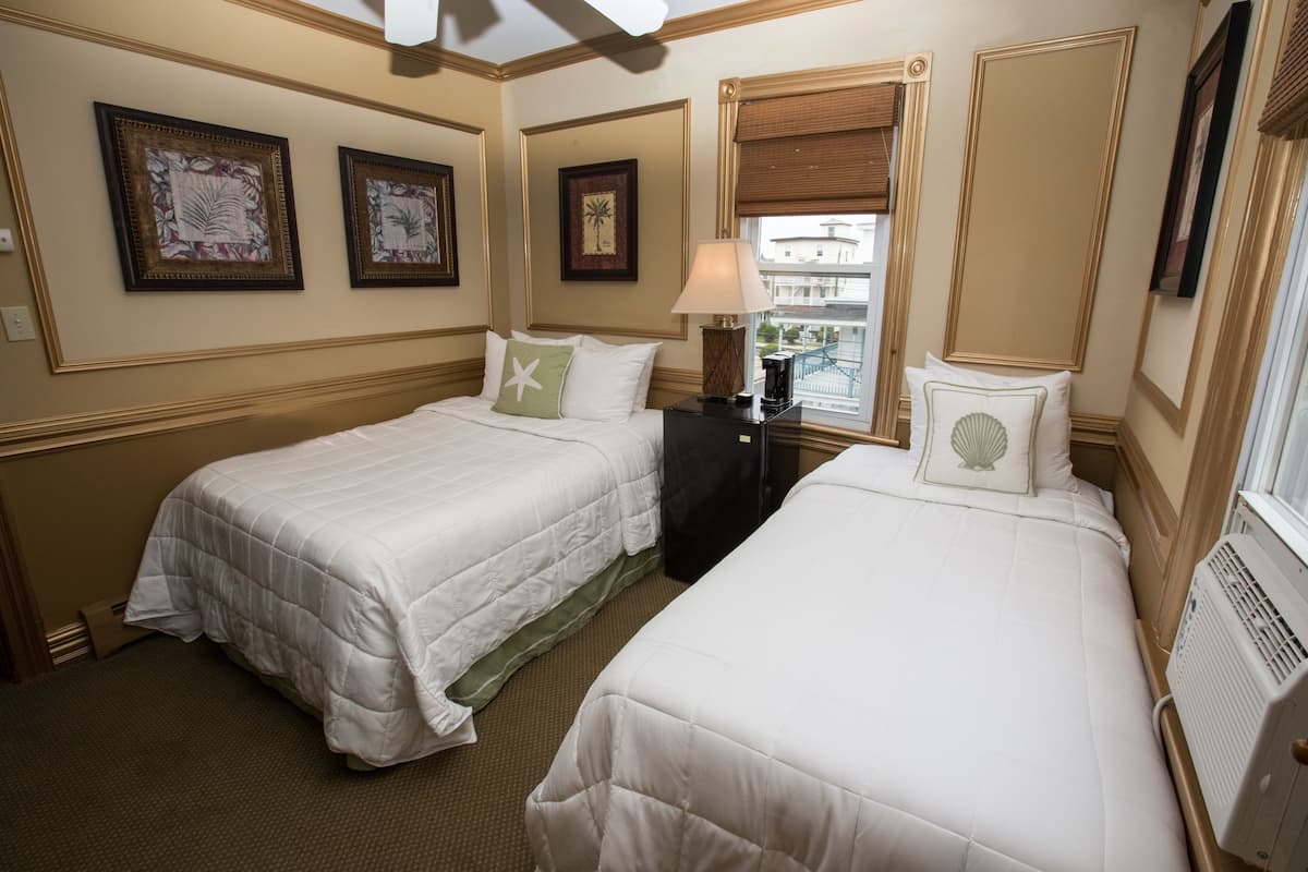 Quarto de hotel com duas camas, janela com vista, obras de arte emolduradas nas paredes e mesa de cabeceira com abajur.
