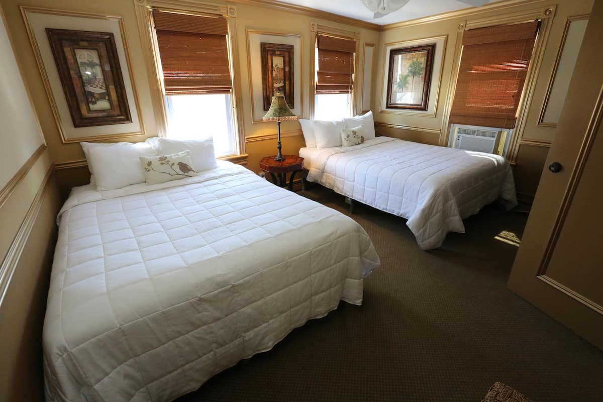 Quarto de hotel com duas camas, uma luminária e uma porta.