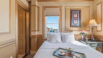 Habitación de hotel con cama, mesita de noche con lámpara, bandeja con juego de té y ventana con vistas a edificios.