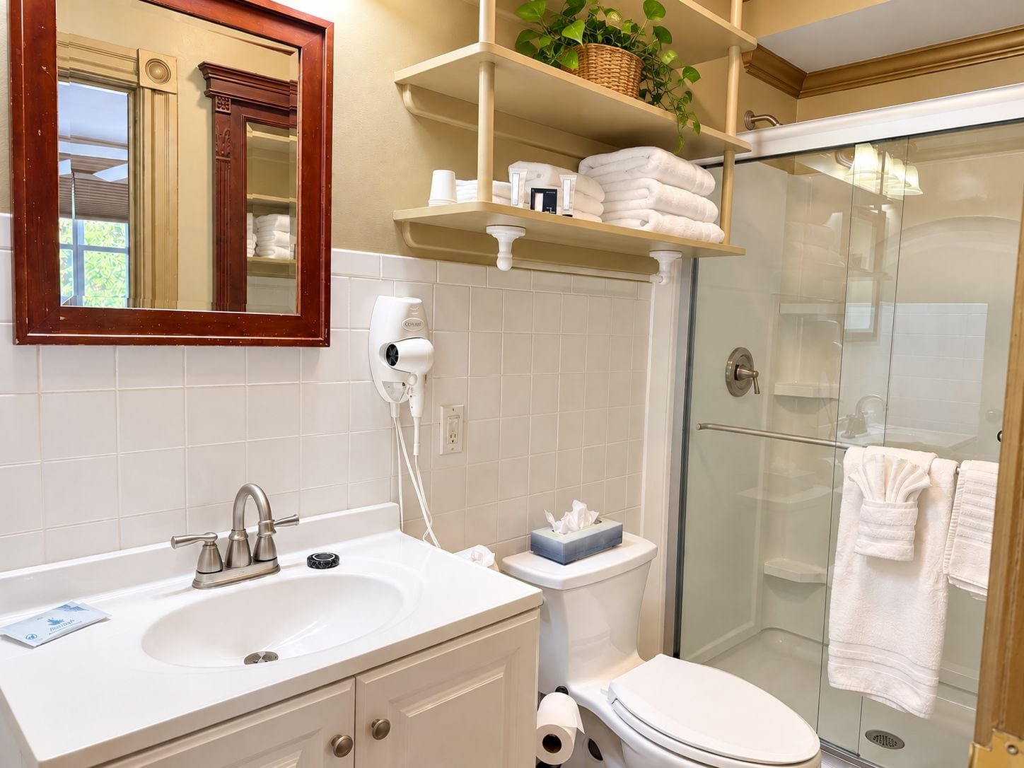 A bathroom with a white sink, a toilet, a glass shower enclosure, and a mirror with a wooden frame.