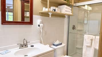 A bathroom with a white sink, a toilet, a glass shower enclosure, and a mirror with a wooden frame.