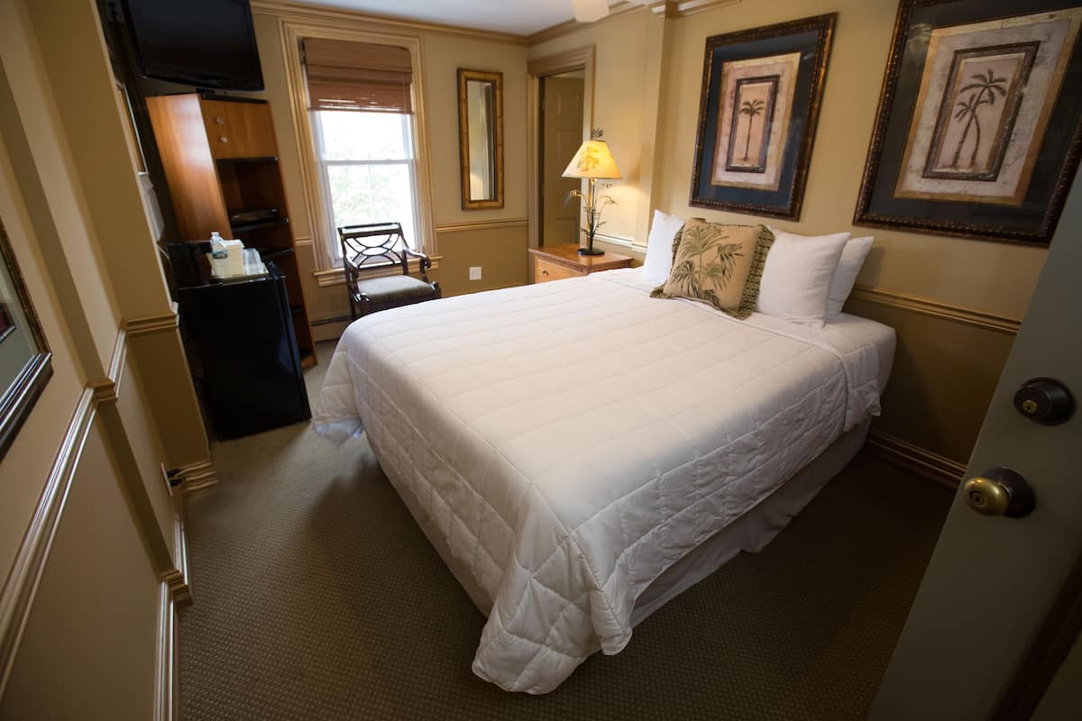 Quarto de hotel com uma cama grande, uma escrivaninha com cadeira, uma luminária e quadros nas paredes.