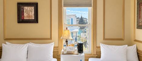 A hotel room with two beds, a window with a city view, a lamp, and a refrigerator.