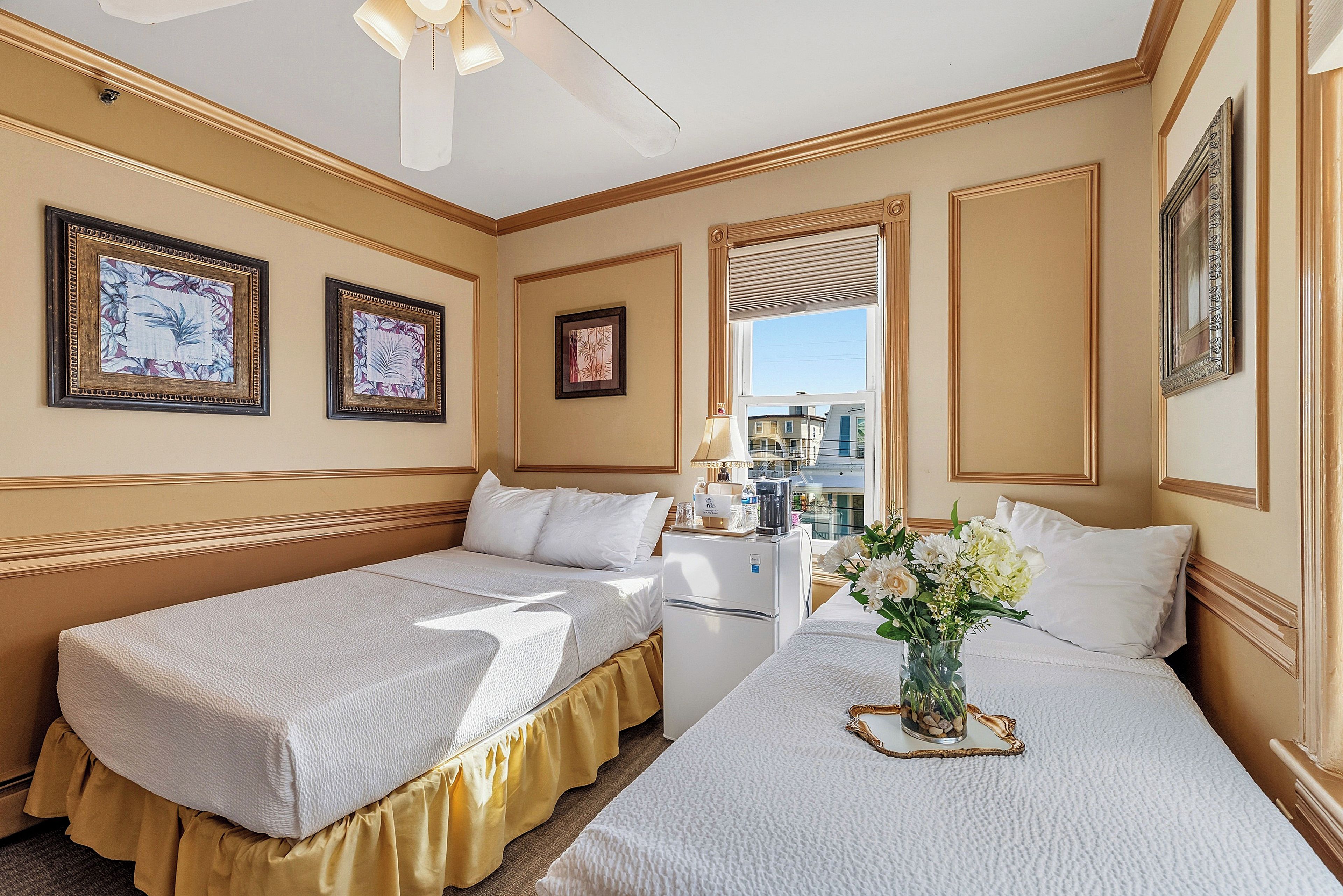 A hotel room with two single beds, a small kitchenette, a window with a view, and decorative wall art.