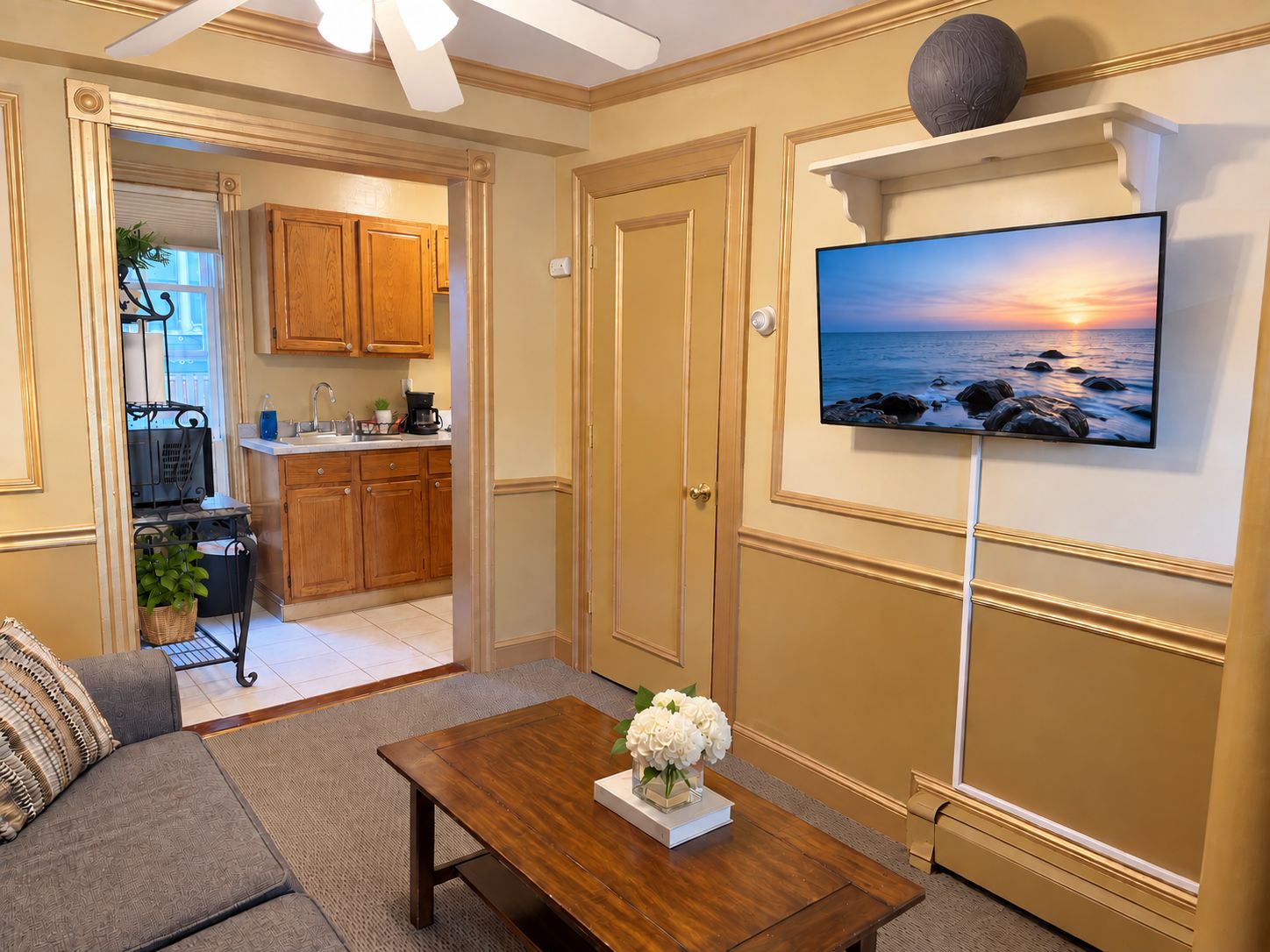 A living room with a sofa, coffee table, and a TV mounted on the wall displaying a sunset view.