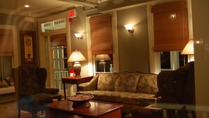 A cozy lobby with a sofa, armchairs, and a coffee table. There are wall sconces and a sign indicating an exit.