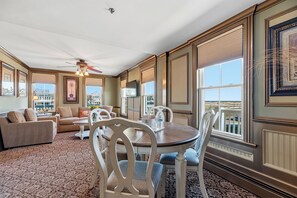 A spacious living room with a ceiling fan, a dining table with chairs, and large windows offering a view of the cityscape. - Ocean View Inn (Ocean Grove)