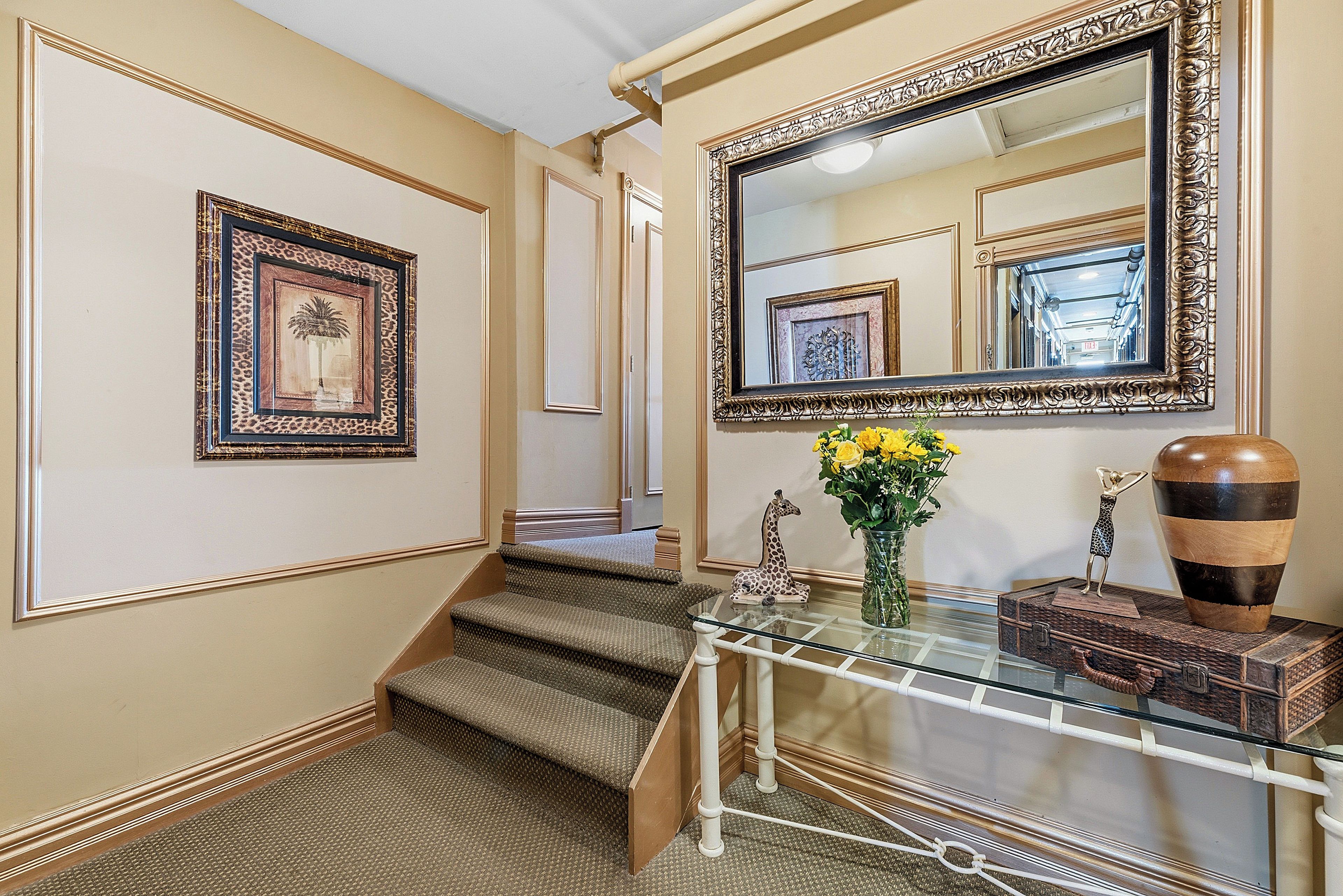 A staircase with carpeted steps, a glass console table with decorative items, and framed artwork on the walls.