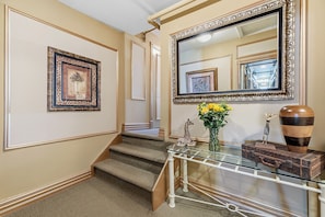A staircase with carpeted steps, a glass console table with decorative items, and framed artwork on the walls.