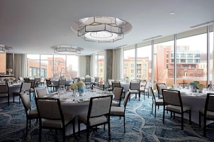 Un comedor amplio con mesas redondas, sillas y ventanas grandes que ofrecen vistas a edificios.