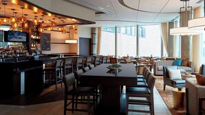 A spacious hotel lobby with a bar area, a large dining table, and comfortable seating. - Ithaca Marriott Downtown on the Commons (Ithaca)