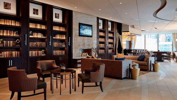A spacious library with bookshelves, a fireplace, comfortable seating, and a television. - Ithaca Marriott Downtown on the Commons (Ithaca)