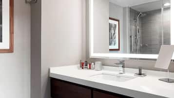 A modern bathroom with a white sink, a large mirror, and a shower area.