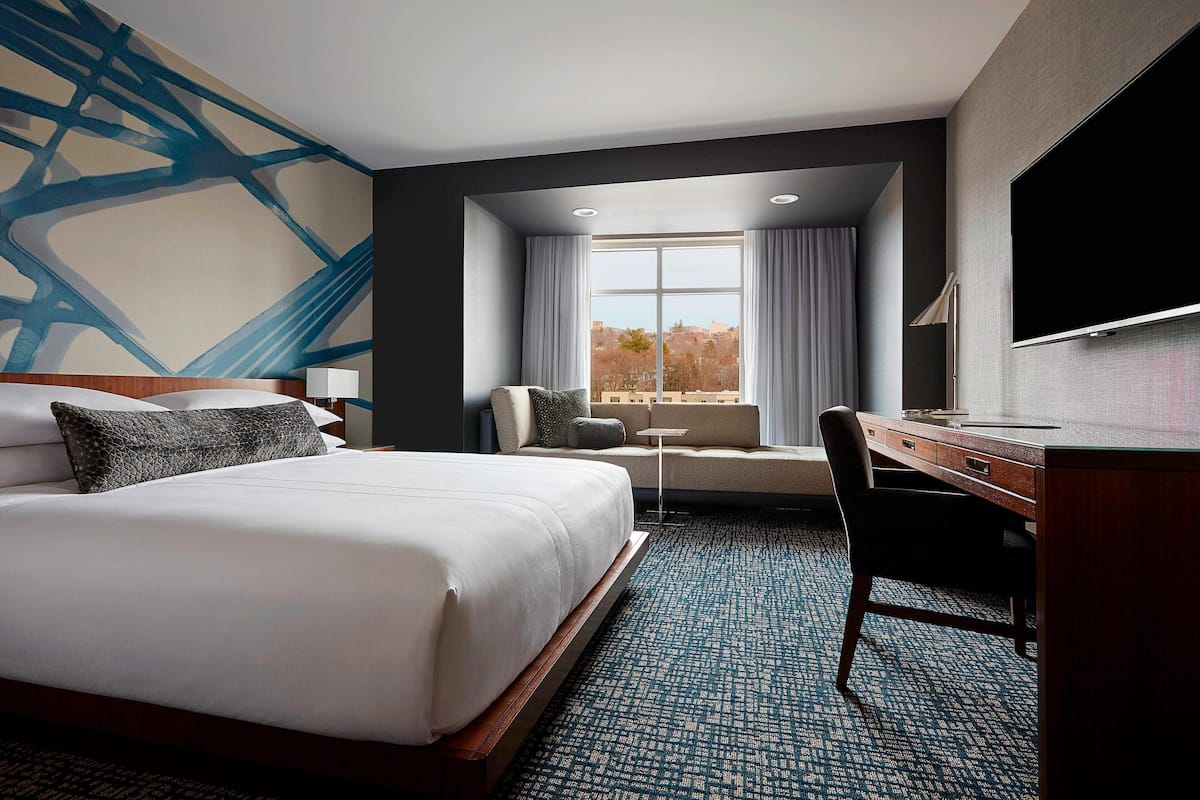 A hotel room with a large bed, a desk, a chair, a television, and a window with curtains.
