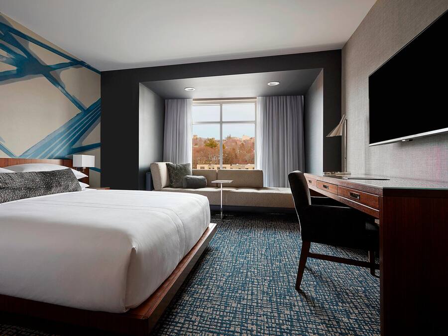 A hotel room with a large bed, a desk, a chair, a television, and a window with curtains.