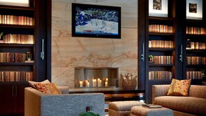 A cozy living room with a fireplace, bookshelves, and a flat-screen TV. - Ithaca Marriott Downtown on the Commons (Ithaca)