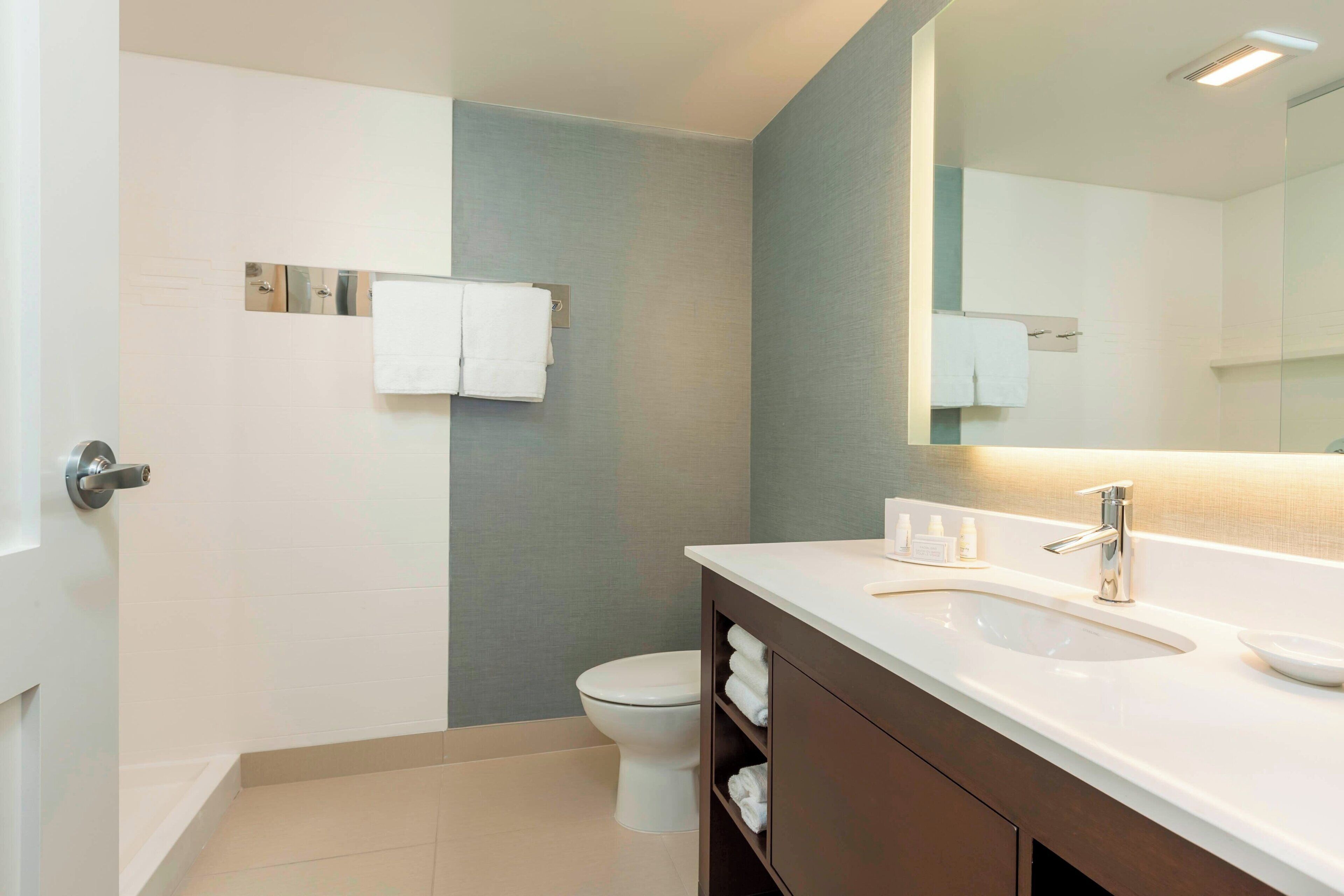 A modern bathroom with a white sink, dark wooden vanity, and a large mirror.