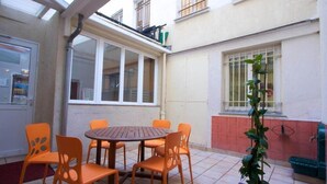 A patio with a round table and orange chairs, a potted plant, and a window with bars. - Auberge Internationale des Jeunes (Paris)