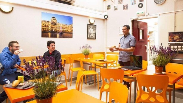 A dining area with orange chairs and tables, a potted plant, and a laptop on a table. - Auberge Internationale des Jeunes (Paris)
