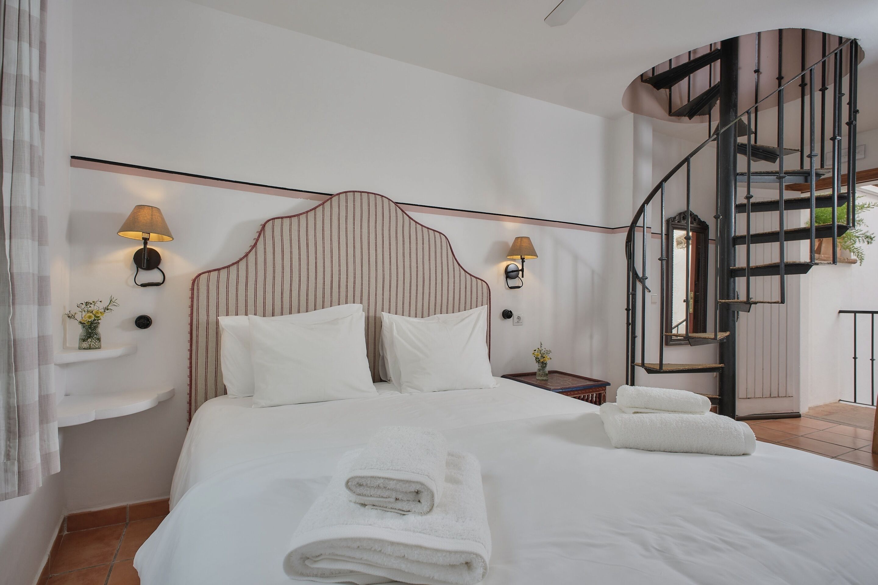 Une chambre à coucher comprenant un lit, deux lampes de chevet, une table de chevet, une étagère murale et un escalier en colimaçon.