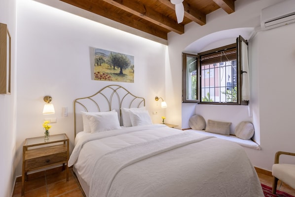 A bedroom with a bed, bedside lamps, a painting, a window with blinds, and a wooden ceiling.