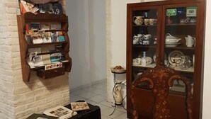 A room with a brick wall, a wooden cabinet with glass doors displaying dishes, a black suitcase, and a patterned rug. - Beni Benius (Cagliari)