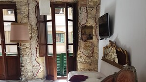 A room with a bed, a vintage armchair, a television, and a stone wall. - Beni Benius (Cagliari)